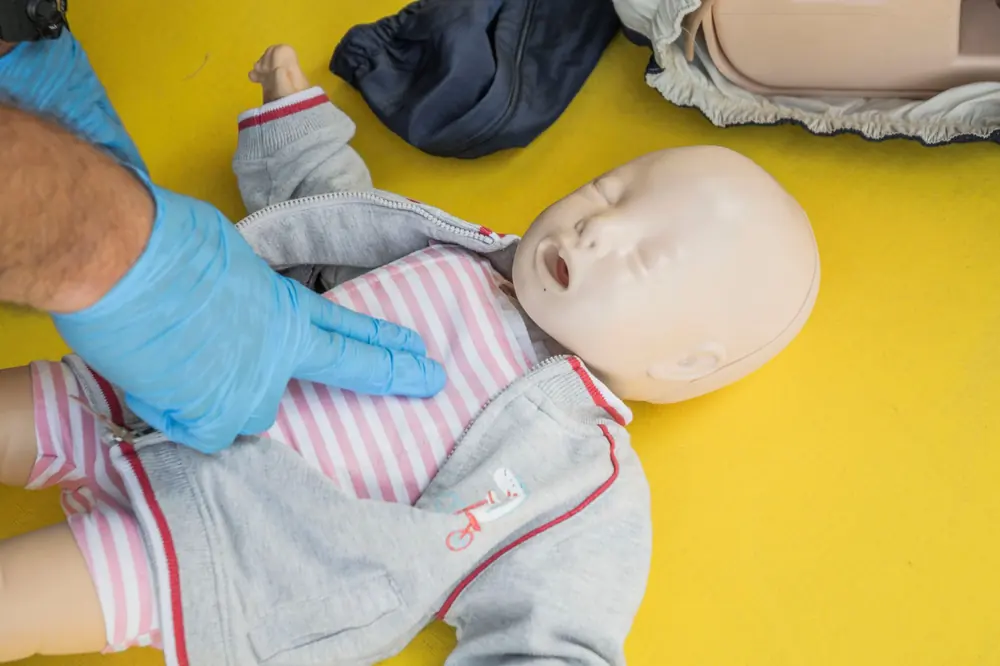 Uciśnięcia klatki piersiowej dwoma palcami na manekinie niemowlęcia